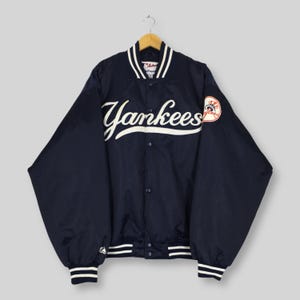 Può includere: Giacca da baseball dei Yankees blu navy con scritte e dettagli bianchi. La giacca presenta il nome della squadra sul petto e una toppa con il logo della squadra sulla manica. Ha una chiusura con bottoni e polsini e colletto a righe.