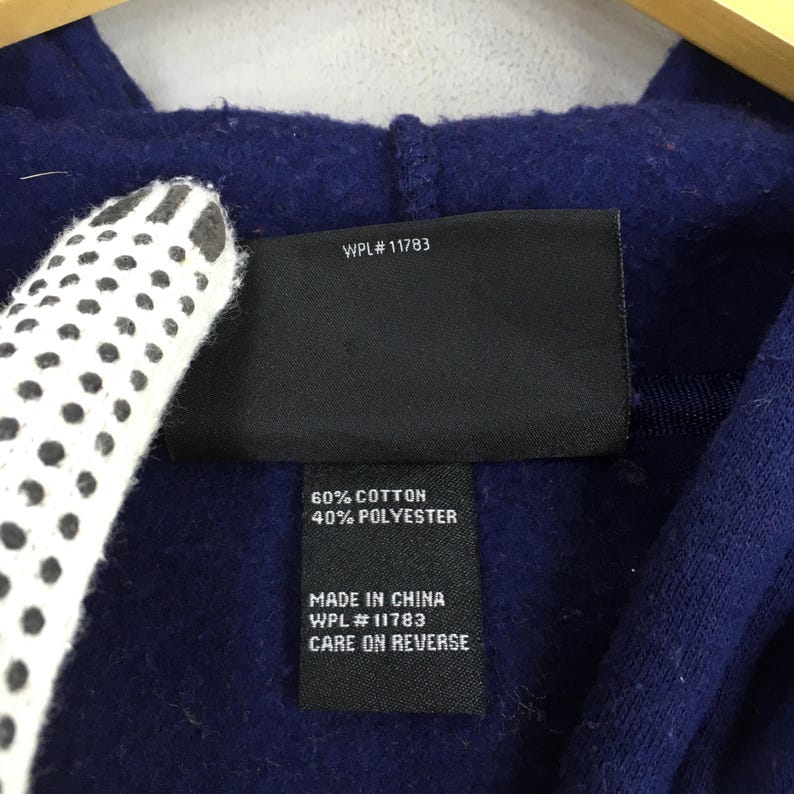 May include: Close-up of a navy blue fabric with a black tag. The tag reads "WPL #11783", "60% COTTON 40% POLYESTER", "MADE IN CHINA", and "CARE ON REVERSE". A white and black patterned object is partially visible.
