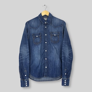 May include: A long-sleeved denim shirt with a classic Western design. The shirt features two chest pockets, a button-down front, and buttoned cuffs. The blue denim has a faded, worn look, and is hanging on a wooden hanger.