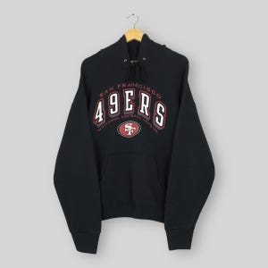 May include: A black hooded sweatshirt featuring the text San Francisco 49ers and National Football League in white and red lettering. The front displays a central 49ers team logo in red, white, and gold, with a drawstring hood and front pocket.
