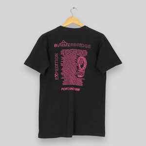 Puede incluir: Camiseta negra con texto y gr&aacute;ficos rosas. La parte posterior de la camiseta presenta las palabras "SUMMERBRIDGE" y "EXPEDITION", junto con una huella de zapato y el texto "PORTLAND 1996".
