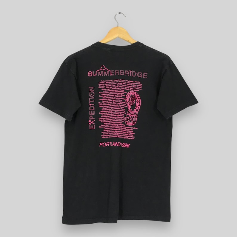 Puede incluir: Camiseta negra con texto y gr&aacute;ficos rosas. La parte posterior de la camiseta presenta las palabras "SUMMERBRIDGE" y "EXPEDITION", junto con una huella de zapato y el texto "PORTLAND 1996".