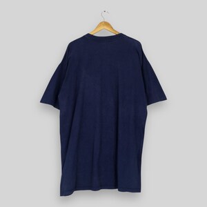 May include: Navy blue t-shirt hanging on a wooden hanger. The short-sleeved shirt is made of a soft material and has a relaxed fit. The back of the shirt is visible, showing the solid color and simple design.