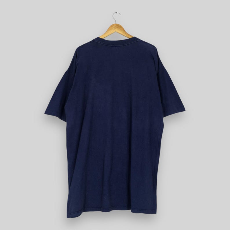 May include: Navy blue t-shirt hanging on a wooden hanger. The short-sleeved shirt is made of a soft material and has a relaxed fit. The back of the shirt is visible, showing the solid color and simple design.