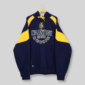 May include: Navy blue hoodie with yellow shoulder and hood panels. The front displays the text "NC A&T SU EST. 1891 AGGIES" in yellow and white. The hoodie has a front pocket and a drawstring hood.