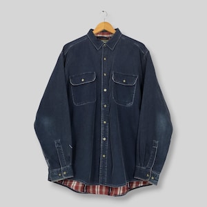 Op de afbeelding: Een overhemd met lange mouwen en knoopsluiting van donkerblauwe denimstof. Het overhemd heeft twee borstzakken met knoopsluiting, een standaard kraag en een zichtbare rood-witte geruite flanellen voering langs de onderzoom en binnenkraag.