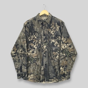 May include: A long-sleeved button-down shirt with a camouflage pattern in shades of green, brown, and black. The shirt has two chest pockets and a button-down collar. The brand name is visible on the collar.