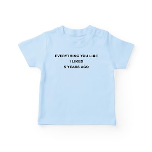 May include: A pale blue t-shirt featuring the black text: "EVERYTHING YOU LIKE I LIKED 5 YEARS AGO". The short-sleeved top is made of a soft fabric. Ideal for everyday wear, this tee is a simple yet bold statement.