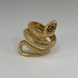 Peut inclure: Une bague dorée en forme de serpent enroulé. La bague présente des écailles détaillées et une tête de serpent relevée. Cette bague est une pièce forte, parfaite pour ajouter une touche de style unique à n'importe quelle tenue.