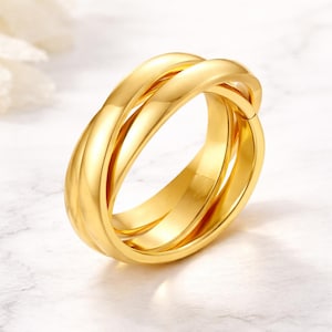 Peut inclure: Une bague dorée avec un design à trois anneaux. Les anneaux sont entrelacés, créant une boucle continue. La bague a une surface polie et réfléchissante, sur un fond doux et neutre. La bague est un bijou.
