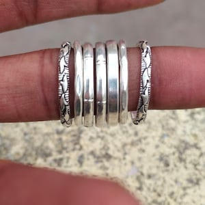 Könnte beinhalten: Eine Sammlung von Silberringen, einige mit glatter, polierter Oberfläche und andere mit detailliertem Blattmuster. Die Ringe werden auf einem Finger präsentiert, um ihre verschiedenen Designs und Texturen hervorzuheben. Die Ringe sind aus Silber.