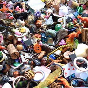 May include: A collection of small, colorful objects including toy dinosaurs, buttons, dice, corks, beads, and playing cards. The items are scattered, creating a textured and diverse display. Various colors and shapes are visible.