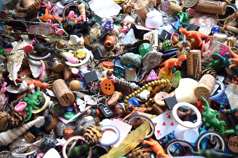 May include: A collection of small, colorful objects including toy dinosaurs, buttons, dice, corks, beads, and playing cards. The items are scattered, creating a textured and diverse display. Various colors and shapes are visible.