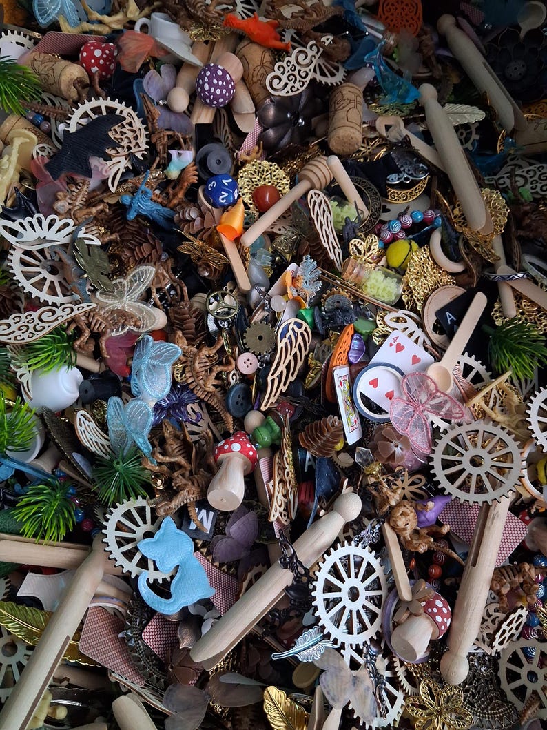 May include: A collection of assorted craft supplies, including wooden gears, miniature mushrooms, playing cards, and decorative wings. The items are in various colors, including red, blue, gold, and white. The image is a close-up shot of the items.