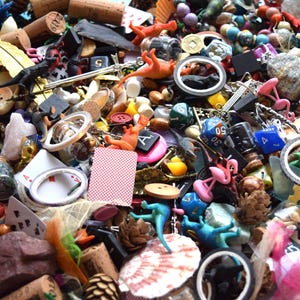 May include: A close-up shot of a collection of small, colorful objects. The assortment includes corks, toy dinosaurs, playing cards, dice, miniature flamingos, and various other trinkets. The items are scattered, creating a visually busy and textured composition.