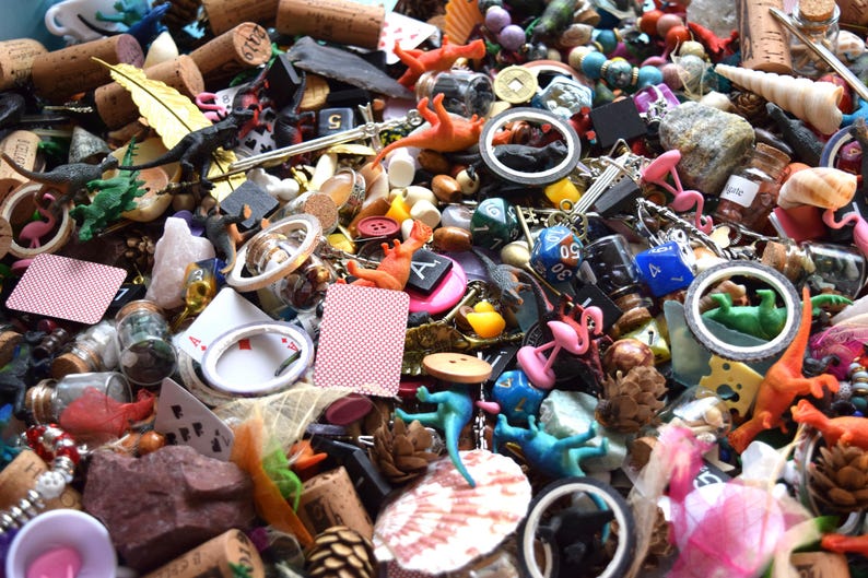 May include: A close-up shot of a collection of small, colorful objects. The assortment includes corks, toy dinosaurs, playing cards, dice, miniature flamingos, and various other trinkets. The items are scattered, creating a visually busy and textured composition.