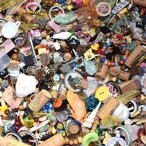 May include: A collection of various small objects, including corks, beads, buttons, shells, and small cups. The items are in a variety of colors and textures, creating a visually diverse assortment. There are also small glass bottles and playing cards.