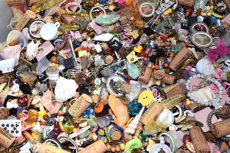 May include: A collection of various small objects, including corks, beads, buttons, shells, and small cups. The items are in a variety of colors and textures, creating a visually diverse assortment. There are also small glass bottles and playing cards.