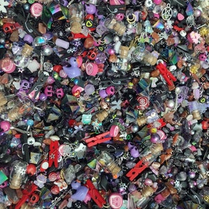 May include: A large assortment of colorful and black charms, beads, and other small decorative items. The items are arranged in a random pattern and include skulls, hearts, stars, and other shapes.