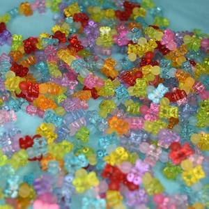 May include: A large pile of colorful gummy bear shaped beads. The beads are translucent and come in a variety of colors, including red, orange, yellow, green, blue, purple, and pink.