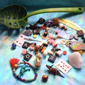 May include: A collection of small decorative items, including a green leaf-shaped serving spoon, playing cards, dice, and miniature figurines. The items are arranged on a light blue surface, creating a whimsical and eclectic display.