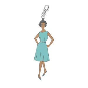 May include: A teal-colored charm featuring a vintage illustration of a woman in a dress, with her hands on her hips. The charm is attached to a silver-colored clasp, suitable for a keychain or bag accessory.