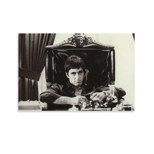 May include: Black and white print of a man seated in a large, ornate chair. He is wearing a dark shirt and has a serious expression. A table with glasses and a bottle is in front of him.