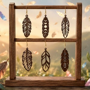 May include: Six dark brown laser-cut wooden feather-shaped earrings hanging from a two-tiered wooden display stand. Each earring features intricate cut-out patterns, including moon phases and geometric designs, suspended by gold-toned metal hooks.
