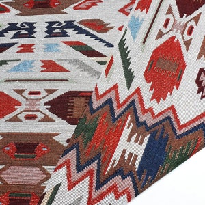 May include: A white fabric with a red, blue, and green geometric pattern. The fabric has a woven texture and is folded in half.