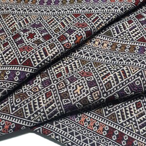 May include: A close-up of a black fabric with a geometric pattern in shades of red, white, and gold. The fabric is folded in half, revealing the intricate details of the design.