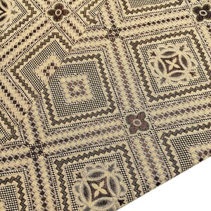 May include: Beige fabric with a brown and black geometric pattern. The pattern features repeating squares and diamonds with intricate details.