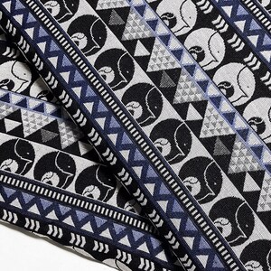 May include: Black and white fabric with a repeating pattern of stylized elephants and triangles. The fabric has a blue and white border.