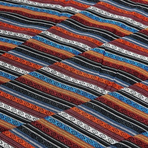 May include: A woven textile with a repeating pattern of diagonal stripes. The stripes feature a variety of colors, including red, orange, blue, white, and black. The design incorporates diamond shapes within the stripes, creating a textured appearance.