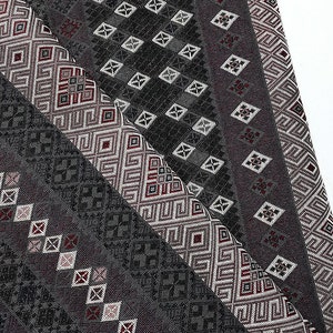 May include: A close-up of a black and white patterned fabric with red accents. The fabric has a geometric design with repeating squares and diamonds.