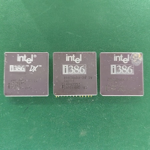 May include: Three square dark gray Intel i386 computer processors arranged in a row. Each chip features the Intel logo and i386 text printed in white. The left chip is marked A80386DX-25, the center is A80386DX-20, and the right is A80386DX-25.