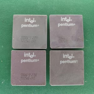 Könnte beinhalten: Vier quadratische, dunkelgraue Intel Pentium Computerprozessoren, die in einem zwei-mal-zwei Raster angeordnet sind. Jeder Prozessor zeigt das weiße Intel Pentium Logo auf der Oberseite sowie verschiedene alphanumerische Codes und das Copyright-Datum 1992-93.