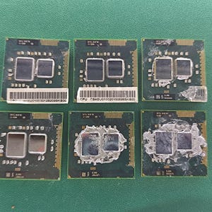 May include: Six square green computer processors arranged in two rows of three. Each unit features two central metallic rectangles, with some showing residual thermal paste. Two processors have white barcode labels with printed text.