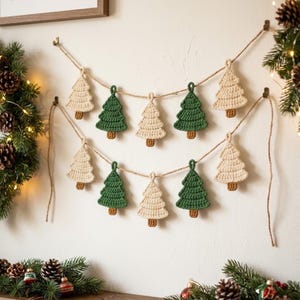 Puede incluir: Una guirnalda de dos niveles con adornos de árboles de Navidad tejidos a ganchillo en colores crema y verde bosque, suspendidos en un cordel de yute natural. Cada árbol tiene un pequeño tronco marrón tejido en la base.