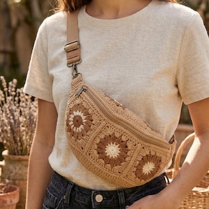 Puede incluir: Un bolso de cintura de ganchillo color beige con un diseño floral. El bolso tiene cierre de cremallera y una correa ajustable. El patrón floral presenta hilo marrón y crema. El bolso se lleva cruzado.
