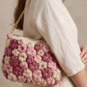 Könnte beinhalten: Eine gehäkelte Handtasche mit strukturiertem Blumenmuster in Creme-, Hellrosa- und Dunkelrosatönen. Die Tasche hat einen goldfarbenen Metallkettenriemen und einen Reißverschluss. Der Text am unteren Bildrand lautet Bonus Free Tote Bag Pattern.
