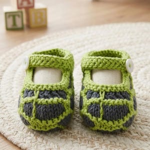 Könnte beinhalten: Ein Paar handgehäkelte Babyschuhe mit einer dunkelgrauen Basis und einem leuchtend hellgrünen Gittermuster. Jeder Schuh verfügt über einen hellgrünen Knöchelriemen mit einem weißen Knopf und eine abgerundete Zehenpartie aus grobem Garn.