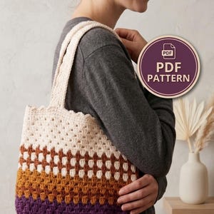 Könnte beinhalten: Eine gehäkelte Tragetasche mit Granny-Square-Muster und horizontalen Farbblöcken in Creme, Rostorange, Senfgelb und Dunkellila. Die Tasche hat zwei passende cremefarbene Häkelgriffe und ein rundes Abzeichen mit der Aufschrift PDF PATTERN.