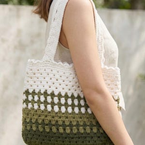 May include: A handmade crochet tote bag with a gradient design. The top and straps are off-white, transitioning to shades of green at the bottom. The bag features a textured, open weave pattern, perfect for carrying everyday items.