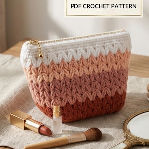 Könnte beinhalten: Eine gehäkelte Tasche mit horizontalen Streifen in Creme, Hellrosa, Altrosa und Terrakotta. Die Tasche hat einen goldfarbenen Reißverschluss mit einem kugelförmigen Zipper. Der Text oben lautet VisualMints PDF CROCHET PATTERN. Die Tasche ist mit einem Lippenstift, einem kleinen Fläschchen, einem Make-up-Pinsel und einem Handspiegel abgebildet.