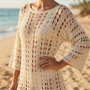 May include: A cream-coloured crochet tunic with a round neckline and three-quarter sleeves. The openwork design reveals the skin beneath. The tunic has a scalloped hemline, suitable for beachwear or as a cover-up.