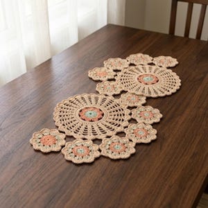 Könnte beinhalten: Ein gehäkelter Tischläufer mit einer Reihe von miteinander verbundenen kreisförmigen Motiven in Beige, Pfirsich und Hellgrün. Das Design besteht aus zwei großen, komplizierten kreisförmigen Medaillons, die von kleineren blumenförmigen Akzenten umgeben sind.