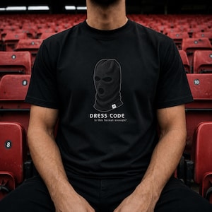 May include: A black short-sleeved t-shirt featuring a graphic of a black balaclava. Below the balaclava, the text reads DRESS CODE and Is this formal enough? The shirt has a small white rectangular tag at the bottom of the balaclava graphic.