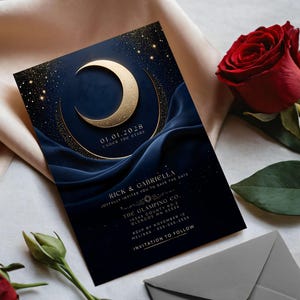 以下が含まれることがあります： 金色の三日月と星のデザインが施された、ネイビーブルーの招待状。カードには日付「01.01.2028」とイベントの詳細が記載されています。赤いバラと灰色の封筒も画像にあります。