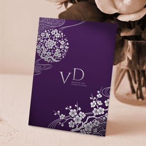 May include: A purple invitation card with silver floral designs and the initials "VD". The card features a large floral circle and smaller floral branches. The text "BOUND BY LOVE, FORGED IN SILVER" is also present.