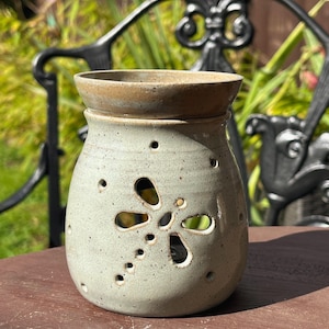 May include: A speckled light green ceramic wax warmer featuring a cutout dragonfly design on the front. The vessel has a wide, bowl-shaped top section for wax melts and a rounded body with small circular perforations surrounding the dragonfly motif.
